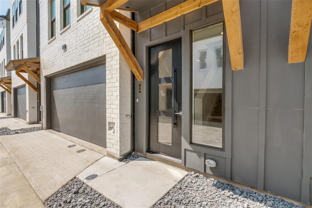 Modern exterior featuring a white brick and gray vertical panel facade, natural wood timber accents, a multi-panel glass entry door, and an attached garage