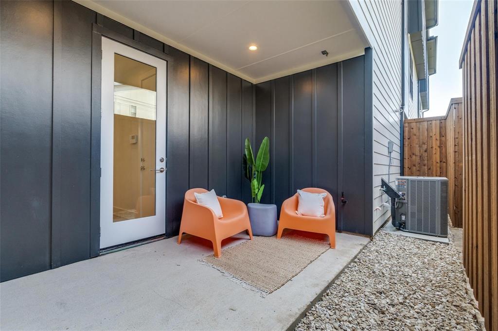 Covered patio with concrete flooring, vertical metal panel siding, full-glass panel door, recessed lighting, and wood-finish privacy fencing