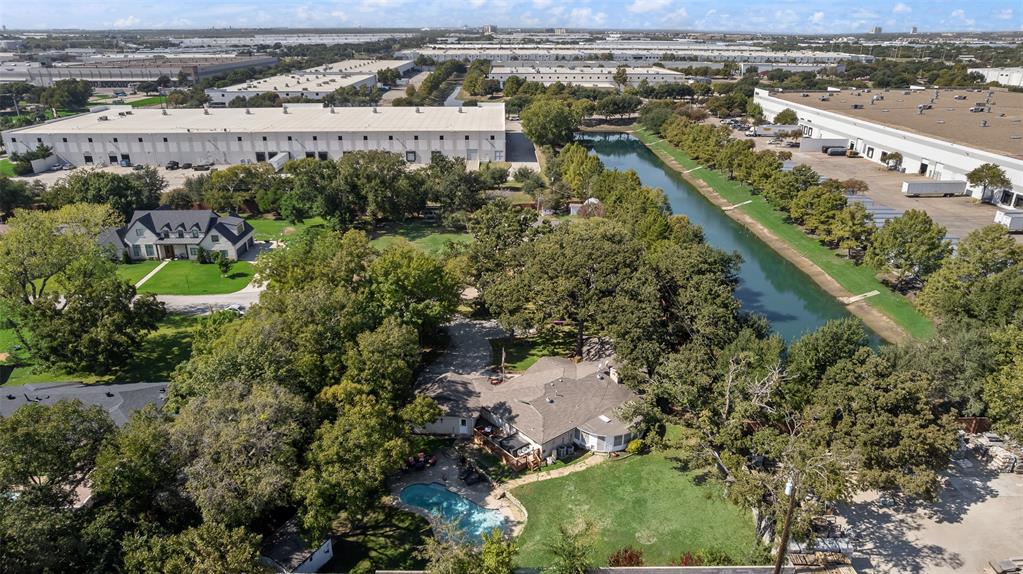 Aerial perspective featuring a residential lot with a swimming pool, mature tree canopy, grass lawn, and waterway frontage