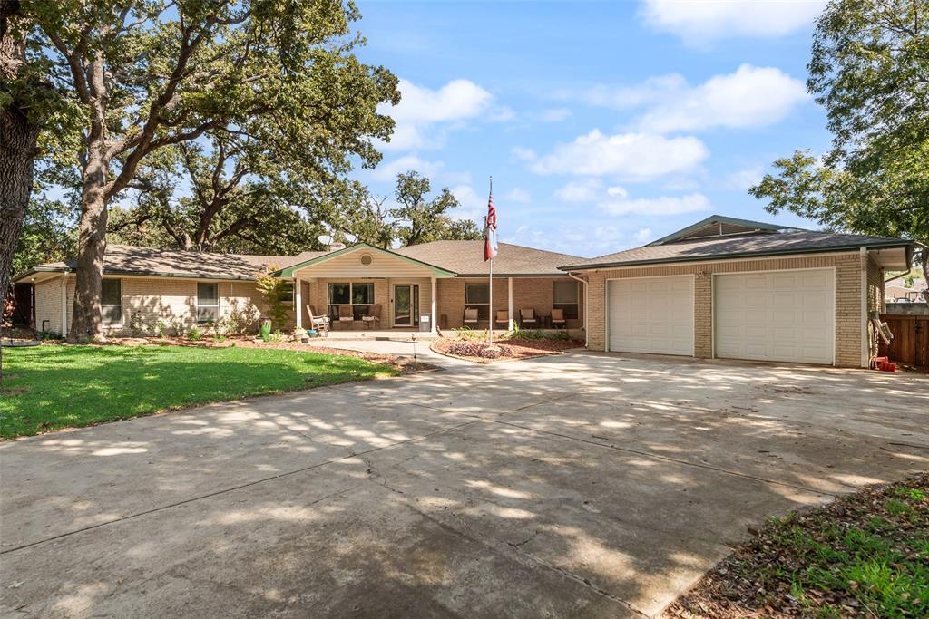 Brick exterior residence featuring a covered front porch, expansive concrete driveway, two-car garage, and mature trees Brick exterior residence featuring a covered front porch, expansive concrete driveway, two-car garage, and mature trees