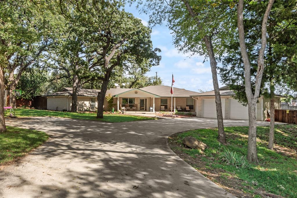 Single-story brick exterior featuring an expansive concrete driveway, attached two-car garage, covered entryway, and mature shade trees Single-story brick exterior featuring an expansive concrete driveway, attached two-car garage, covered entryway, and mature shade trees