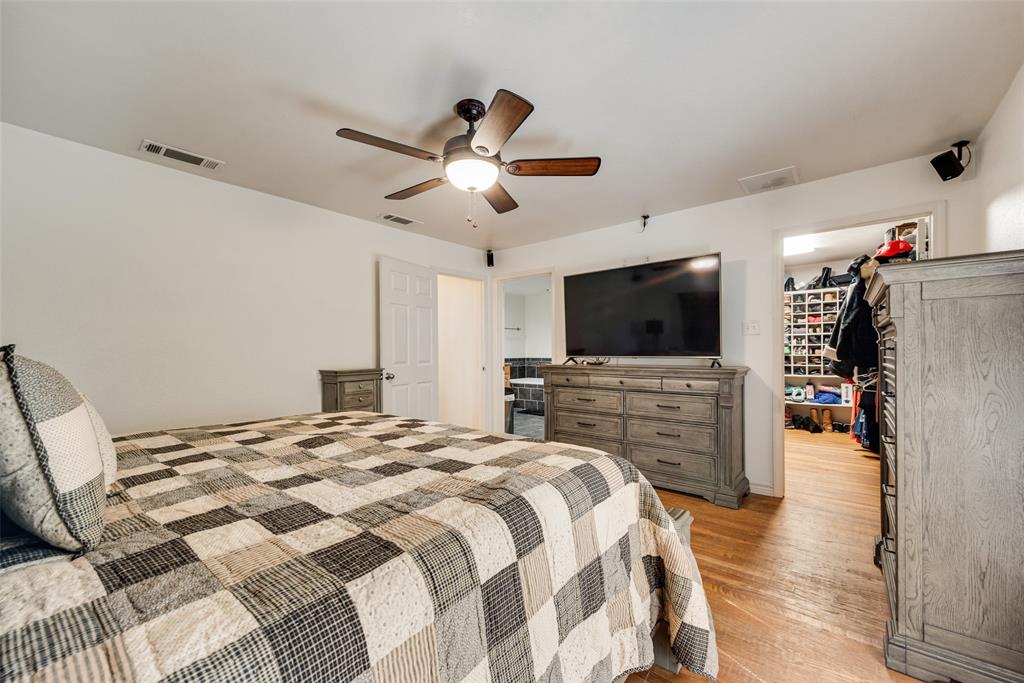 Room featuring wood-finish flooring, a ceiling fan with integrated lighting, and a walk-in closet with built-in shelving