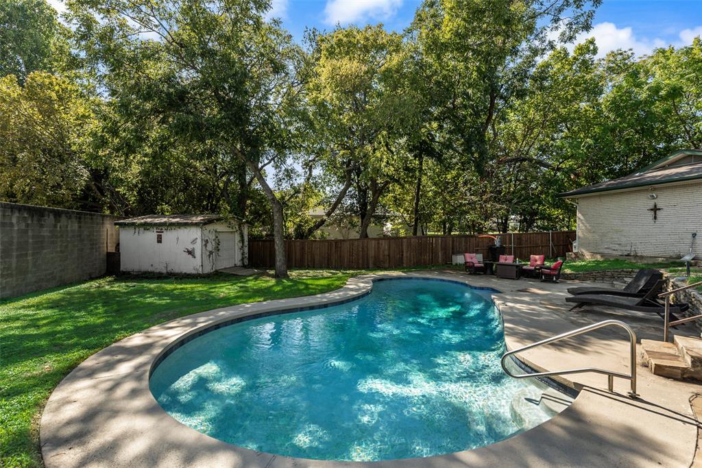Backyard featuring an inground pool with concrete decking, a detached storage structure, wooden perimeter fencing, and mature trees
