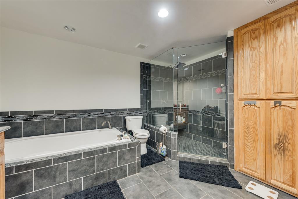 Bathroom featuring a soaking tub with tile surround, walk-in glass-enclosed shower with tile finishes, and built-in floor-to-ceiling wood cabinetry