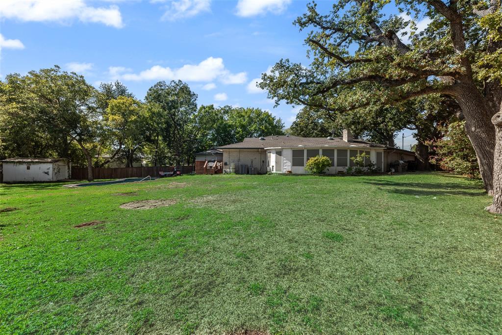 Expansive backyard featuring mature trees, a grass lawn, a detached storage structure, and a fenced perimeter