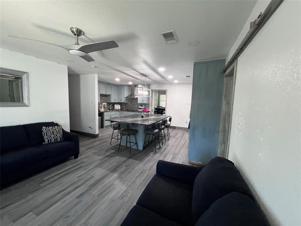 Wood-finish flooring throughout, kitchen featuring a central island with stone countertop, stainless steel range hood, recessed lighting, and sliding barn door hardware