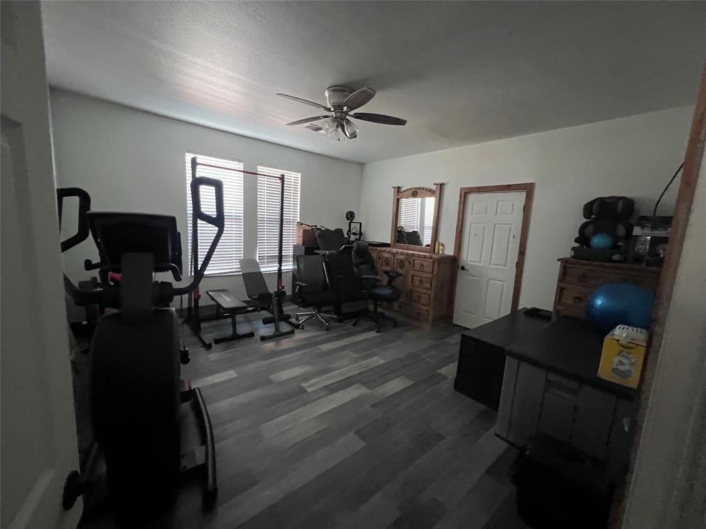 Room featuring multi-tone wood-finish flooring, dual windows with integrated blinds, and a ceiling-mounted light fixture with fan blades