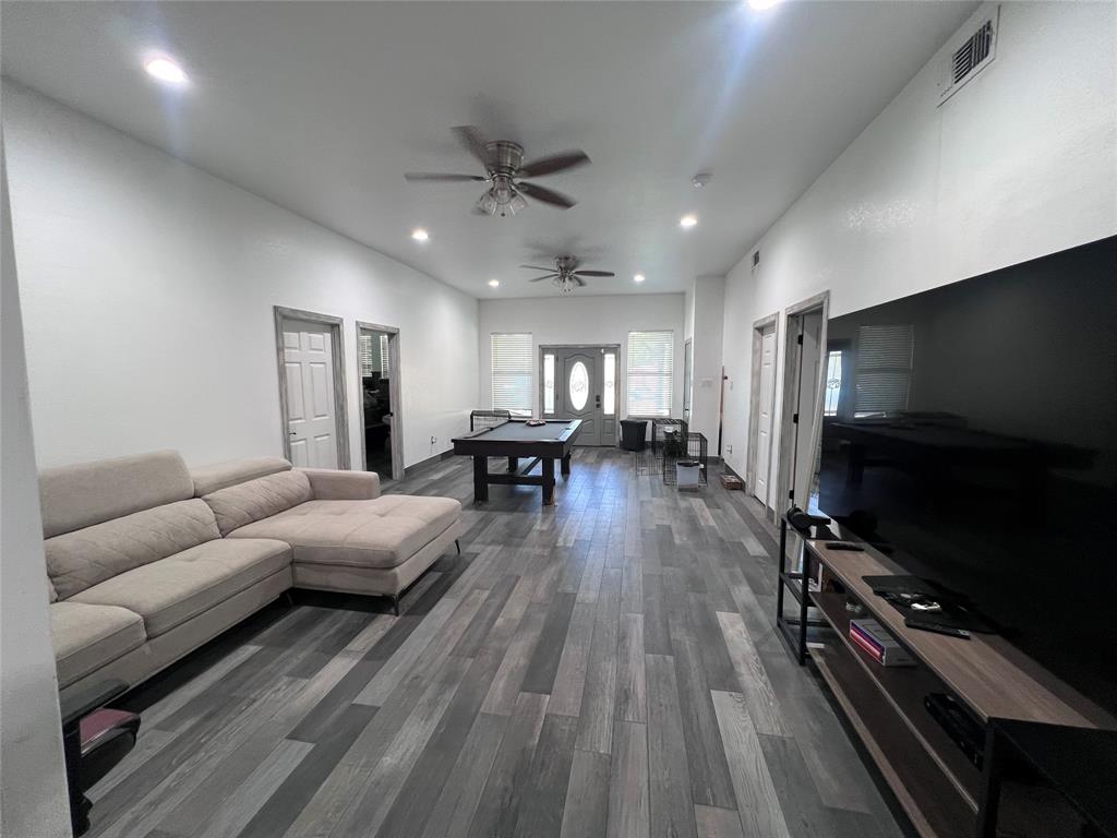 Neutral-toned wood-finish flooring, recessed ceiling lighting, two dual-blade ceiling fans, and a multi-panel front door with an oval glass insert