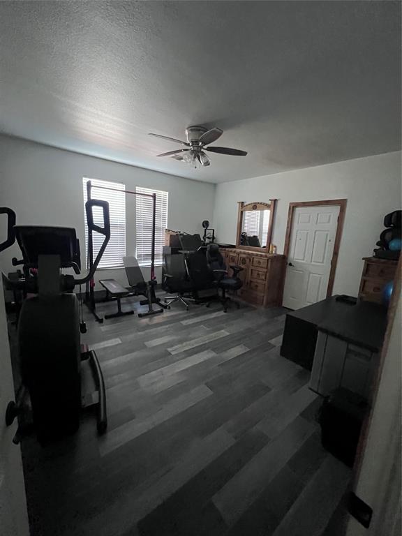 Room featuring wood-finish flooring, dual windows with horizontal blinds, and a central ceiling fan