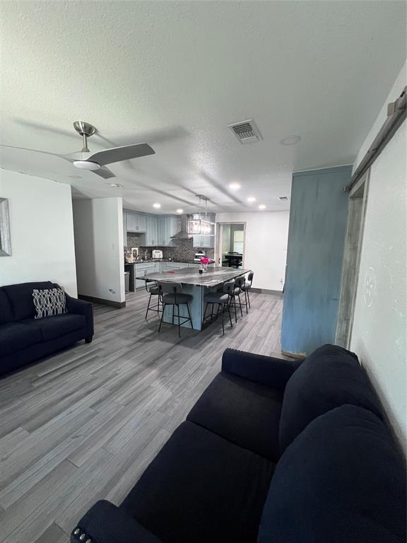 Open-concept kitchen featuring an expansive center island with stone-finish countertop, stainless steel range hood, recessed lighting, and wood-finish flooring