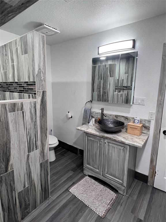 Vanity featuring a stone-finish countertop, vessel sink, and metallic faucet, complemented by wood-finish flooring and a tiled partition wall with decorative mosaic inlay