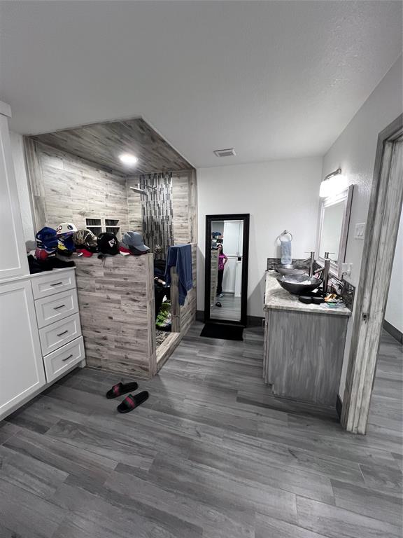 Custom vanity with dual vessel sinks and stone-finish countertop, wood-finish flooring throughout, and a walk-in shower featuring wood-finish tile surround and built-in shelving