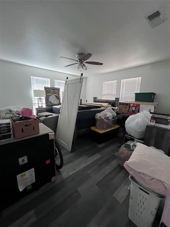 Room featuring wood-finish flooring, a ceiling fan with integrated lighting, and multiple windows with horizontal blinds