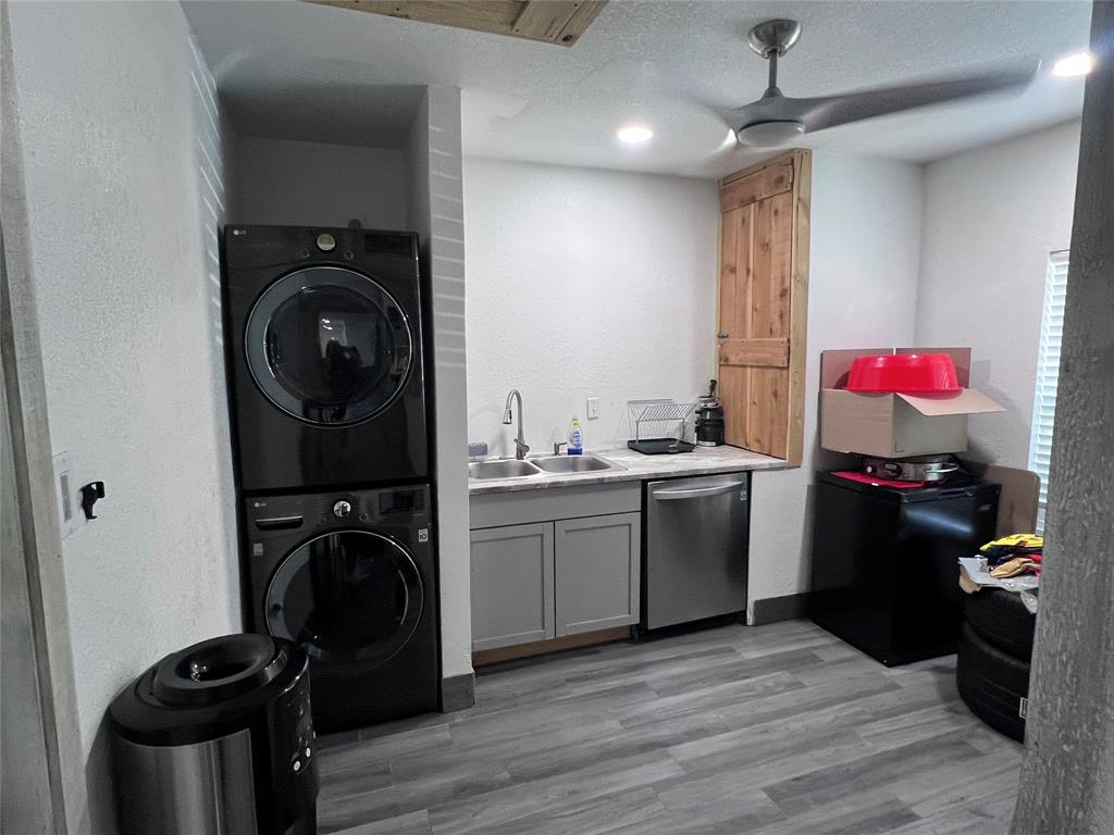 Utility area featuring wood-finish flooring, shaker-style cabinetry, stainless steel sink with pull-down faucet, and built-in wood-paneled storage