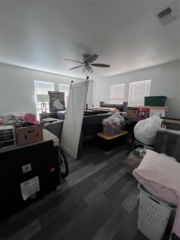 Room featuring wood-finish flooring, four windows with blinds, and a ceiling fan with integrated lighting