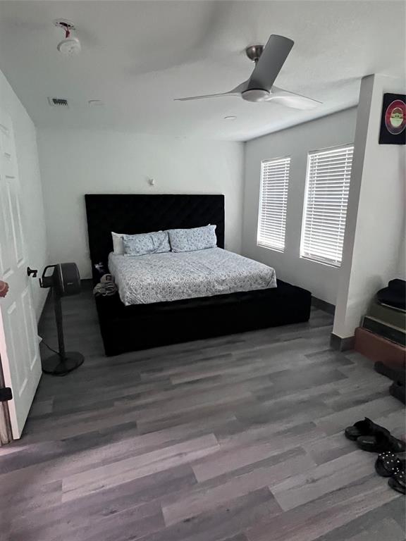 Wood-finish flooring, dual windows with blinds, and a modern ceiling fan with integrated lighting