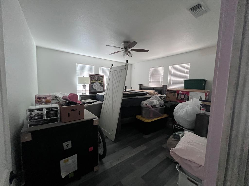 Neutral interior featuring wood-finish flooring, white walls, four windows with horizontal blinds, and a ceiling fan with light fixture