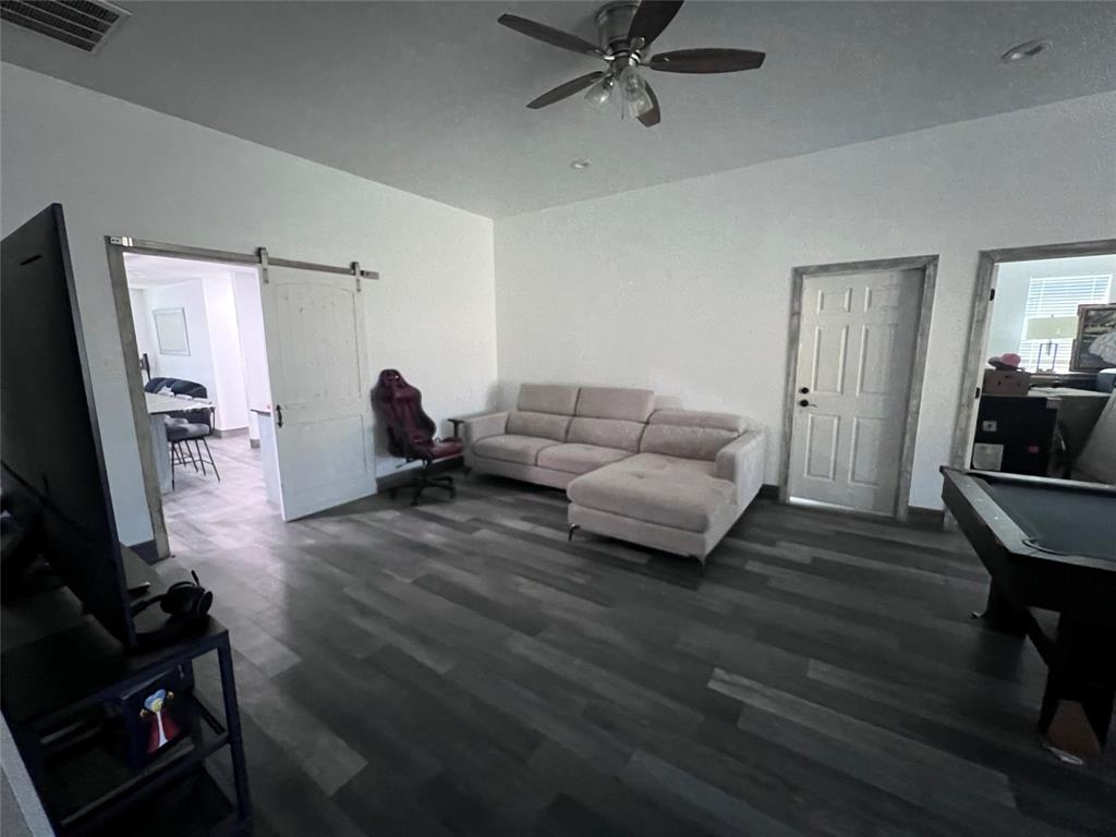 Living space featuring wood-finish flooring, a white sliding barn door, recessed lighting, a ceiling fan with integrated light fixture, and interior doors with decorative trim
