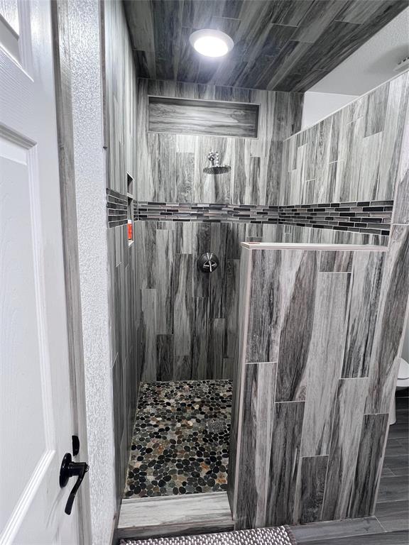 Walk-in shower featuring wood-finish tile wall cladding, a decorative glass mosaic tile accent border, recessed wall niche, and natural stone pebble floor tiling