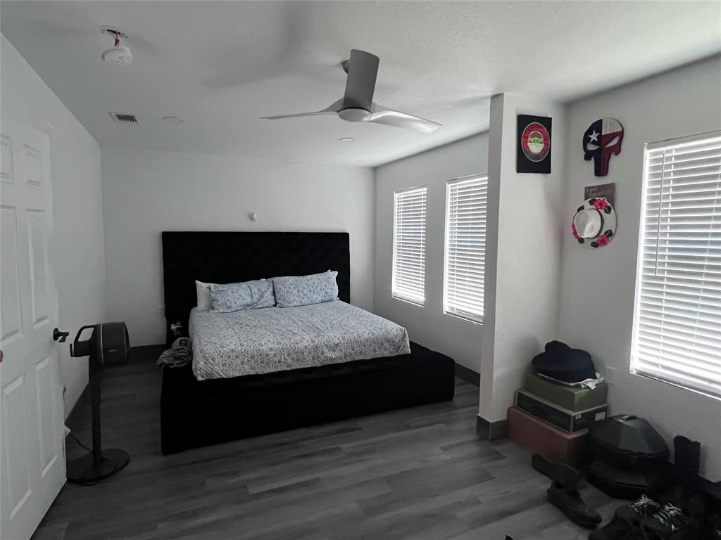 Bedroom featuring wood-finish flooring, three windows with horizontal blinds, and a modern ceiling fan Bedroom featuring wood-finish flooring, three windows with horizontal blinds, and a modern ceiling fan