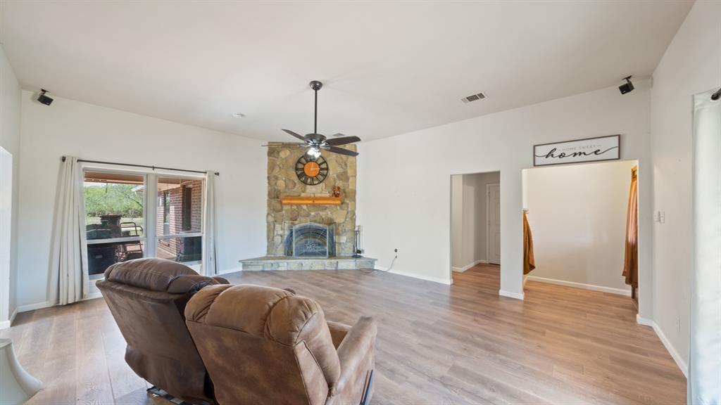 High ceilings featuring a central fan, stone-surround fireplace with a hearth, and wood-finish flooring