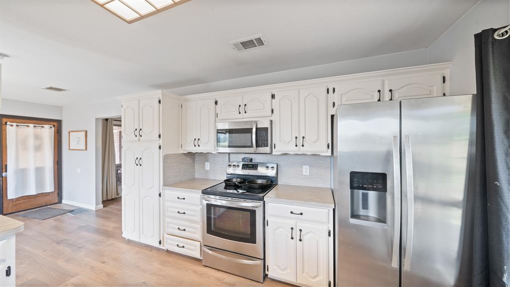 Kitchen featuring painted cabinetry, stainless steel appliances, neutral countertops, and wood-finish flooring