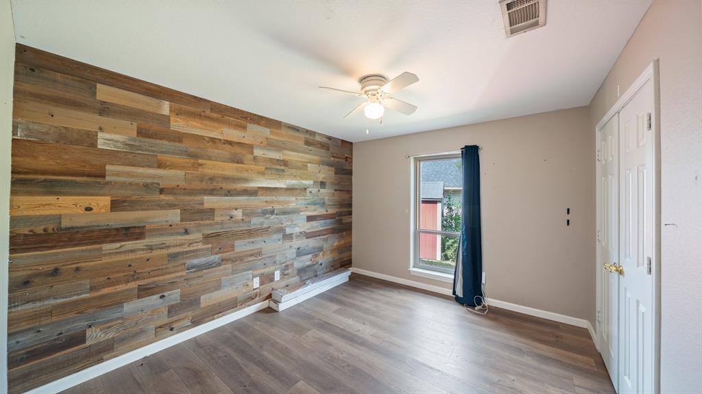 Wood-plank accent wall featuring varied natural textures, wood-finish flooring, ceiling fan with integrated lighting, and white six-panel closet doors