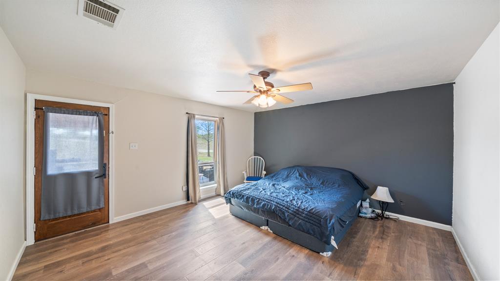 Wood-finish flooring, dark grey accent wall, ceiling fan with integrated lighting, and wooden exterior door with glass insert