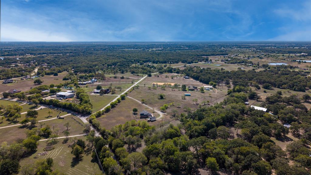 Aerial perspective of expansive acreage featuring mature tree clusters, open pasture land, and established gravel road access