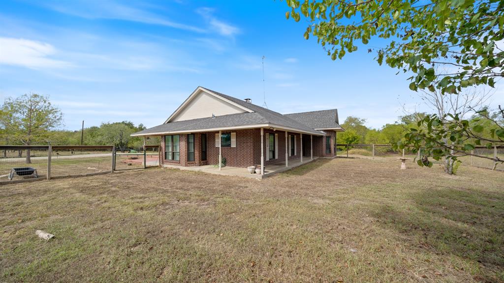 Single-story brick exterior featuring a wrap-around covered porch, gabled roofline, and post-and-rail perimeter fencing