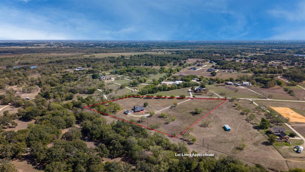 Aerial perspective of a large acreage lot featuring expansive open grass fields, mature trees, and a residential structure