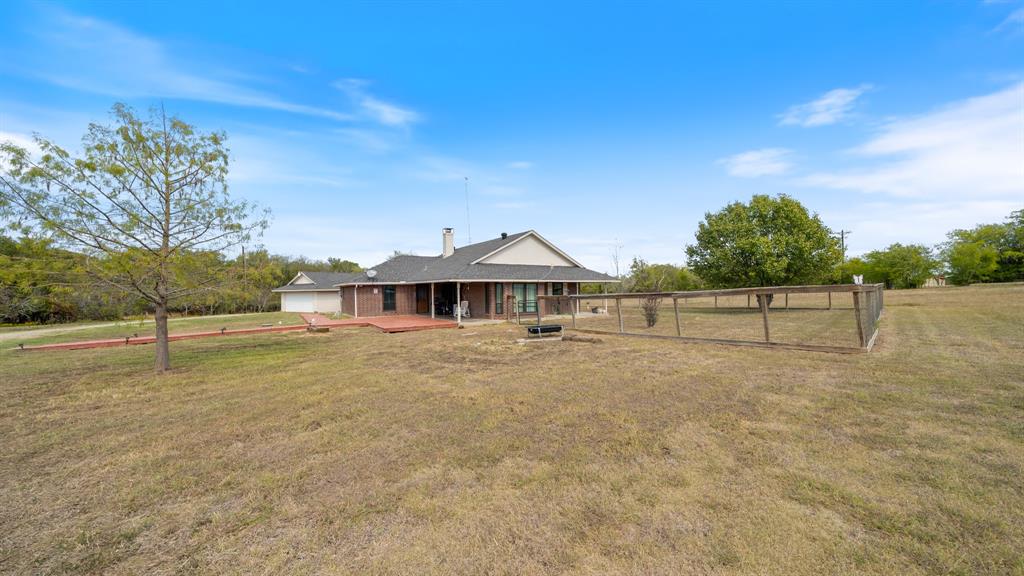Single-story brick exterior residence featuring a covered patio, attached garage, and perimeter wire fencing on an expansive acreage lot