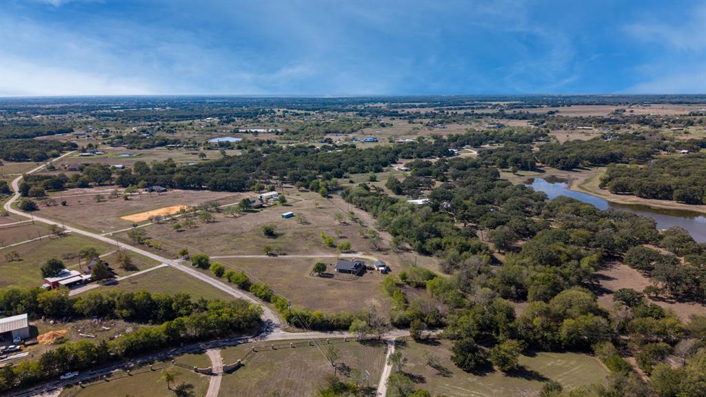 Aerial view of acreage featuring mature tree lines, open pasture, and a water feature