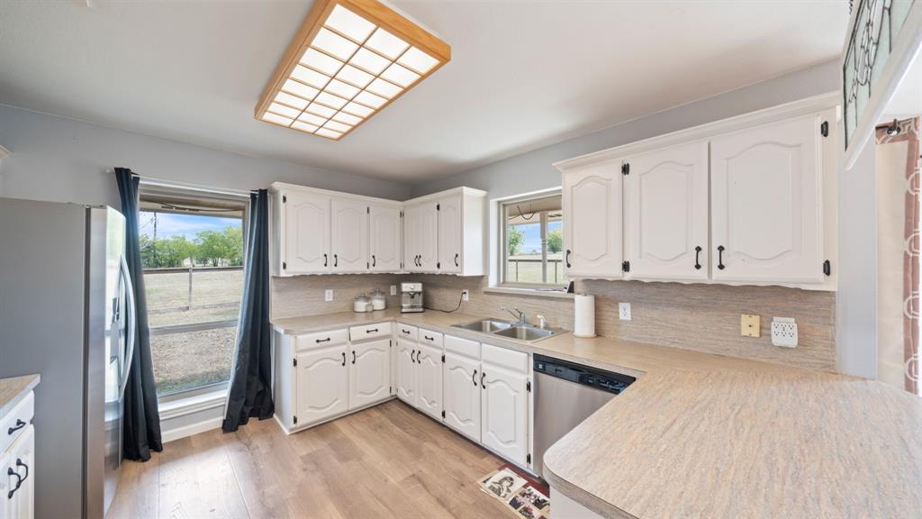 Kitchen featuring white cabinetry with dark hardware, laminate countertops, stainless steel dual-basin sink, stainless steel dishwasher, and wood-finish flooring