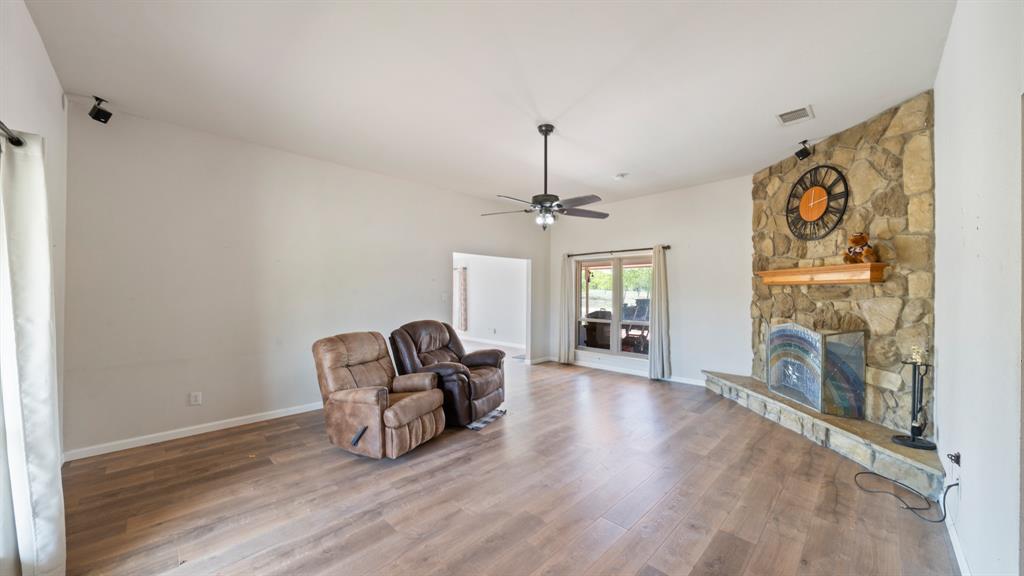 Living area featuring wood-finish flooring, a floor-to-ceiling stone fireplace with a raised hearth, a wooden mantel, and a ceiling fan