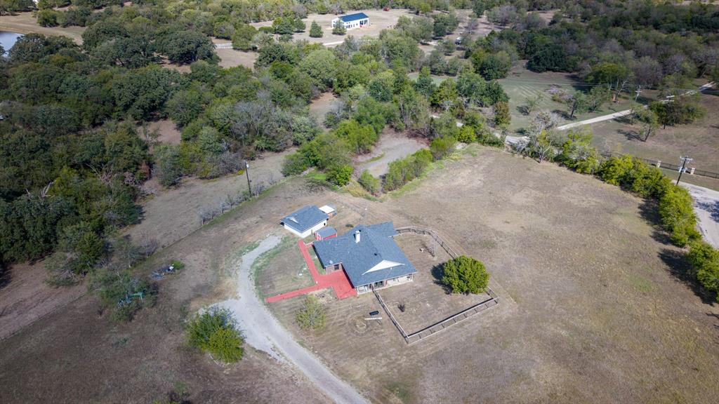 Aerial perspective of a sprawling property featuring a detached structure, gravel driveway, segmented perimeter fencing, and mature trees across an expansive lot