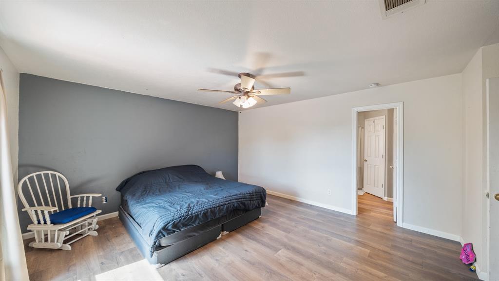 Room featuring wood-finish flooring, a neutral color palette with a slate-toned accent wall, and a multi-light ceiling fan
