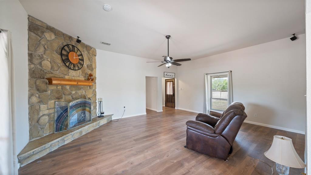 Floor-to-ceiling stone fireplace with a prominent hearth and wooden mantel, wood-finish flooring, high ceilings, and a ceiling fan