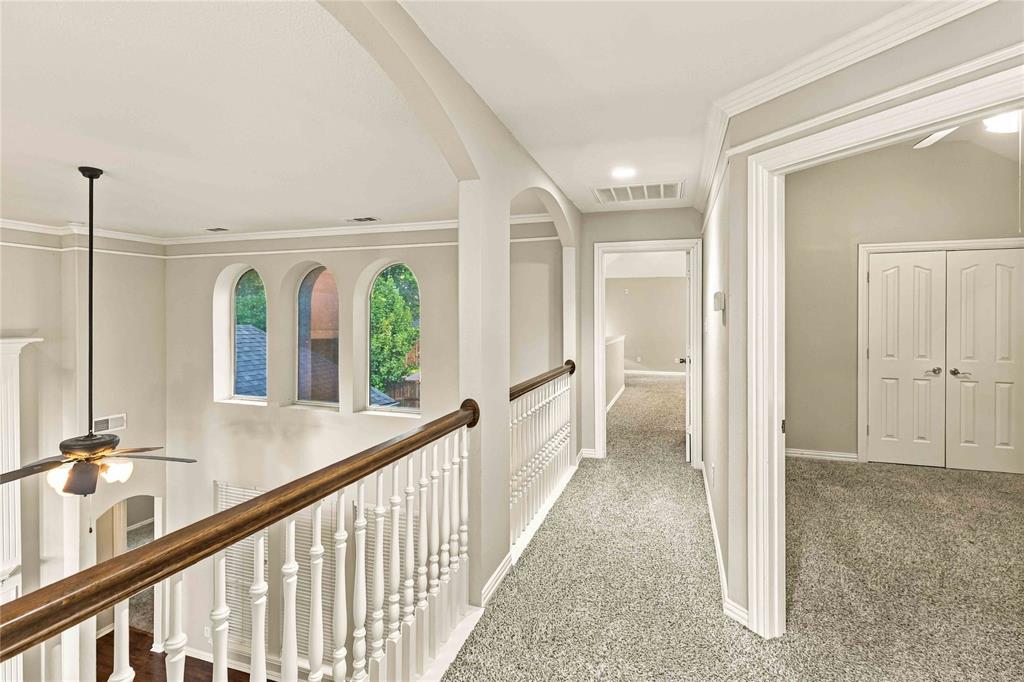 Interior balcony featuring decorative arched wall cutouts, wood-topped railing with white balusters, recessed lighting, and crown molding
