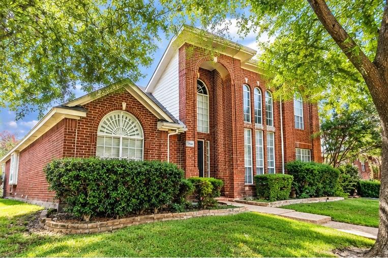 Two-story brick exterior featuring an arched entryway, decorative fanlight windows, and stone-bordered landscaping