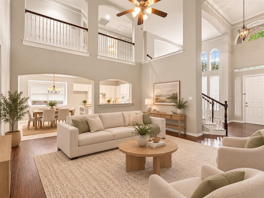 Two-story living area featuring vaulted ceilings, arched architectural detailing, dark wood-finish flooring, a ceiling fan, and multi-level balconies with decorative railings