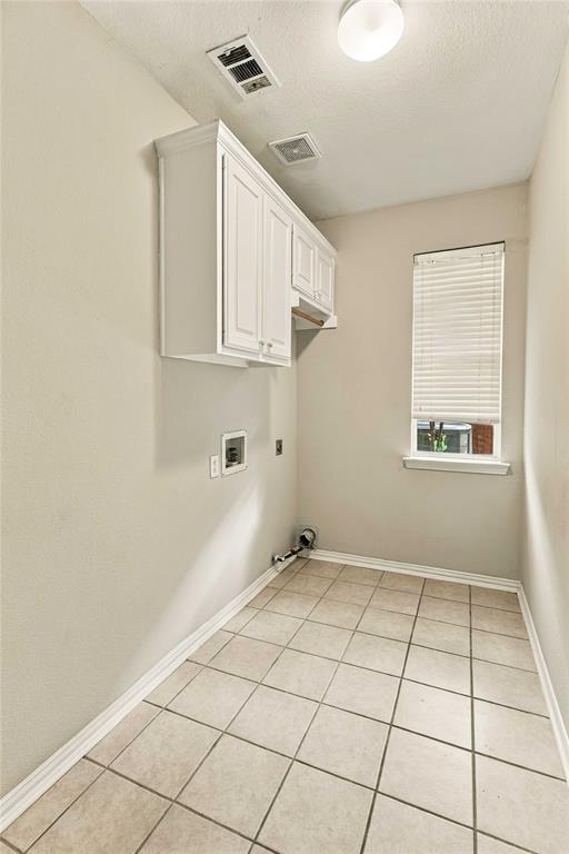 Utility room featuring neutral ceramic tile flooring, white shaker-style wall-mounted cabinetry, and a window with horizontal blinds
