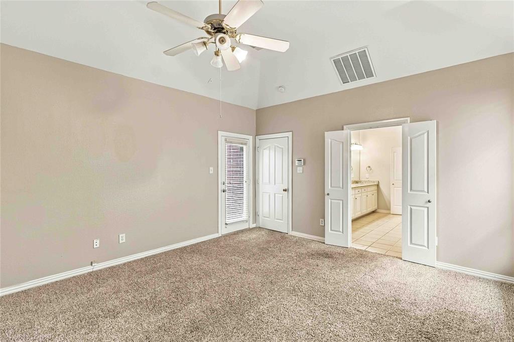 Vaulted ceilings with a central multi-blade ceiling fan, neutral wall tones, carpeted flooring, and double doors opening to a secondary space