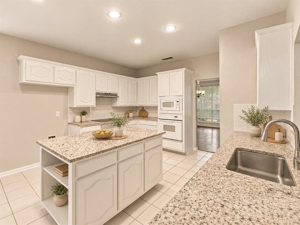 Kitchen featuring white cabinetry, stone-finish countertops, a central island with integrated shelving, built-in wall oven and microwave, and ceramic tile flooring