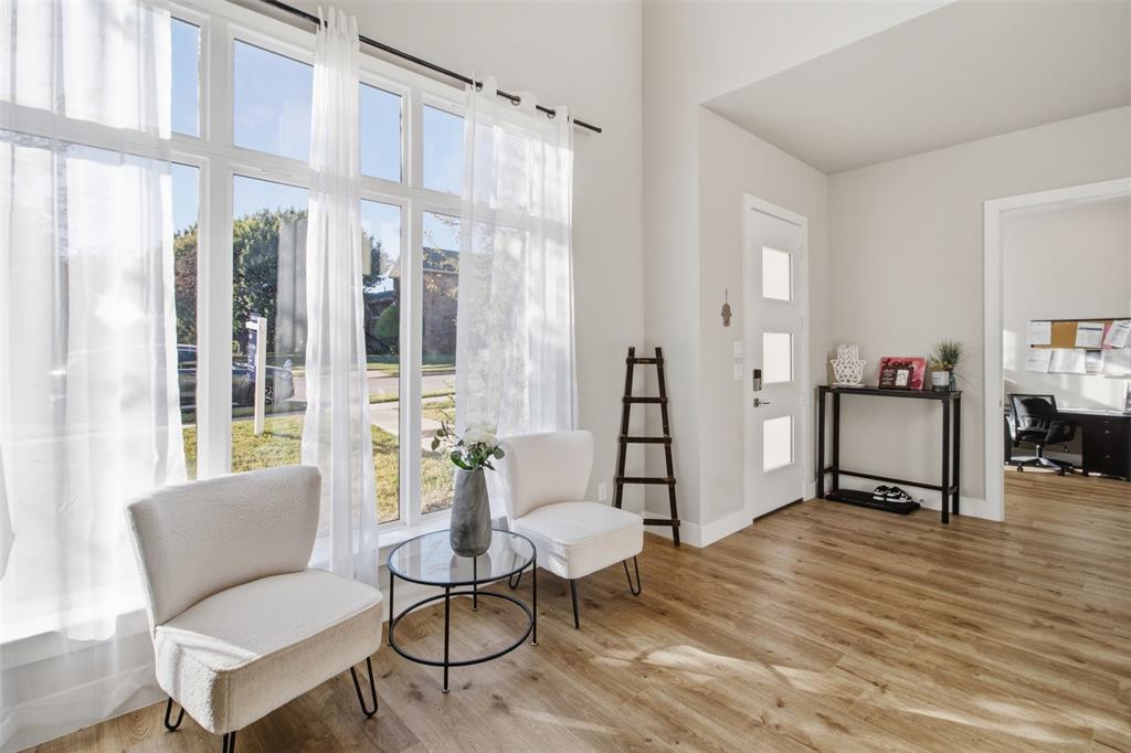 Vaulted ceiling, expansive floor-to-ceiling windows, white entry door with frosted glass panels, and wood-finish flooring
