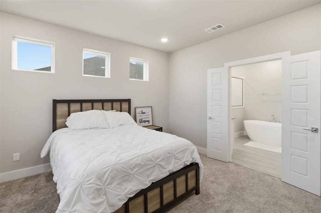 Neutral-toned interior featuring three high-placed windows, neutral carpeting, recessed ceiling lighting, and double doors opening to a space with a soaking tub