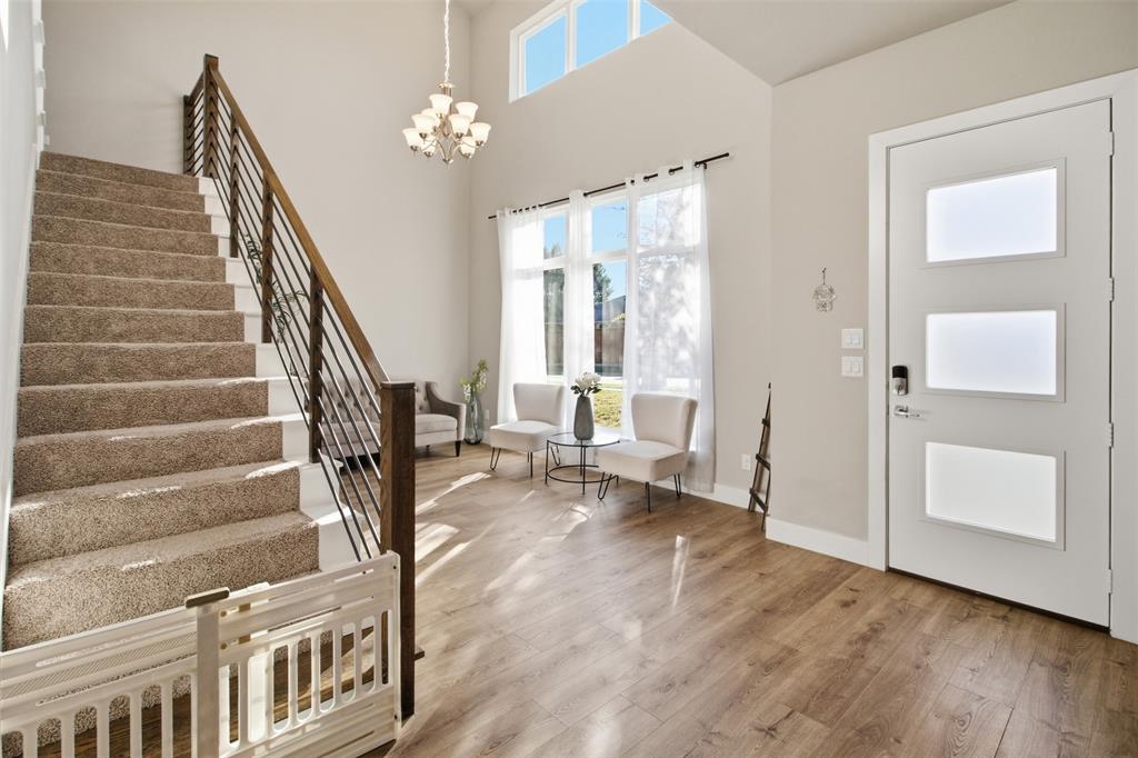 Foyer featuring high ceilings, wood-finish flooring, a staircase with horizontal metal railing, multi-pane transom and full-length windows, and a glass-paneled entry door