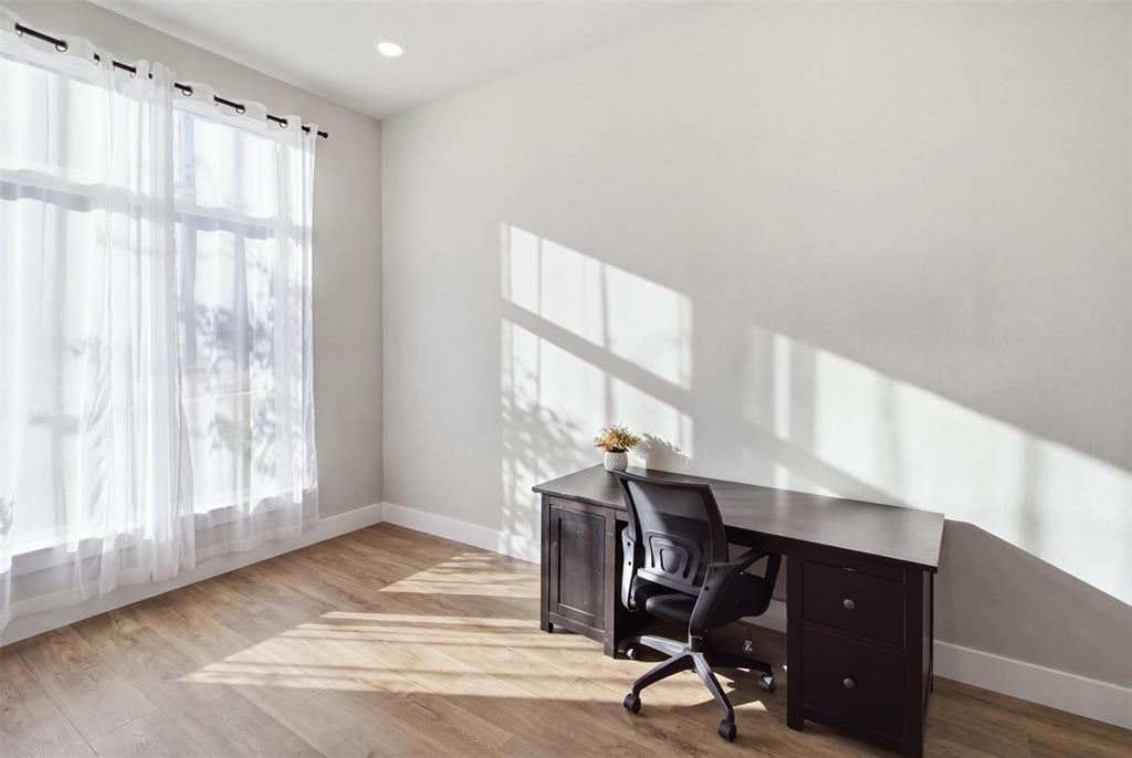 Room featuring wood-finish flooring, neutral wall paint, and a large window with tall glass panels, illuminated by recessed ceiling lighting