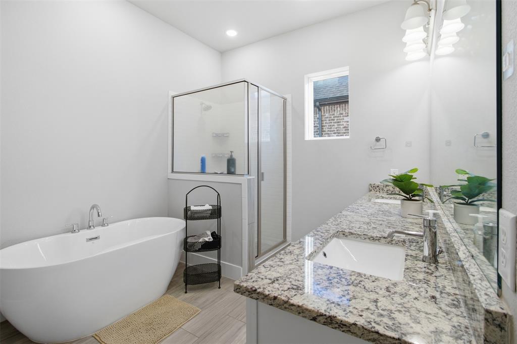 Freestanding soaking tub, glass-enclosed shower, dual-sink vanity with stone countertop, tile flooring, and oversized vanity mirror