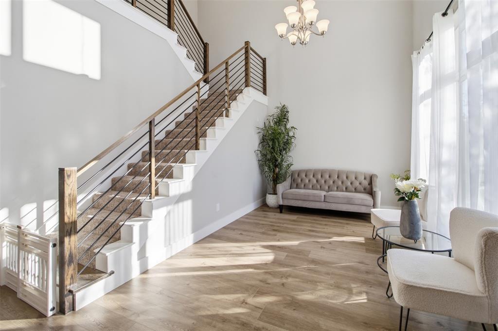 Double-height foyer featuring wood-finish flooring, a grand staircase with horizontal cable railing, and a multi-arm chandelier